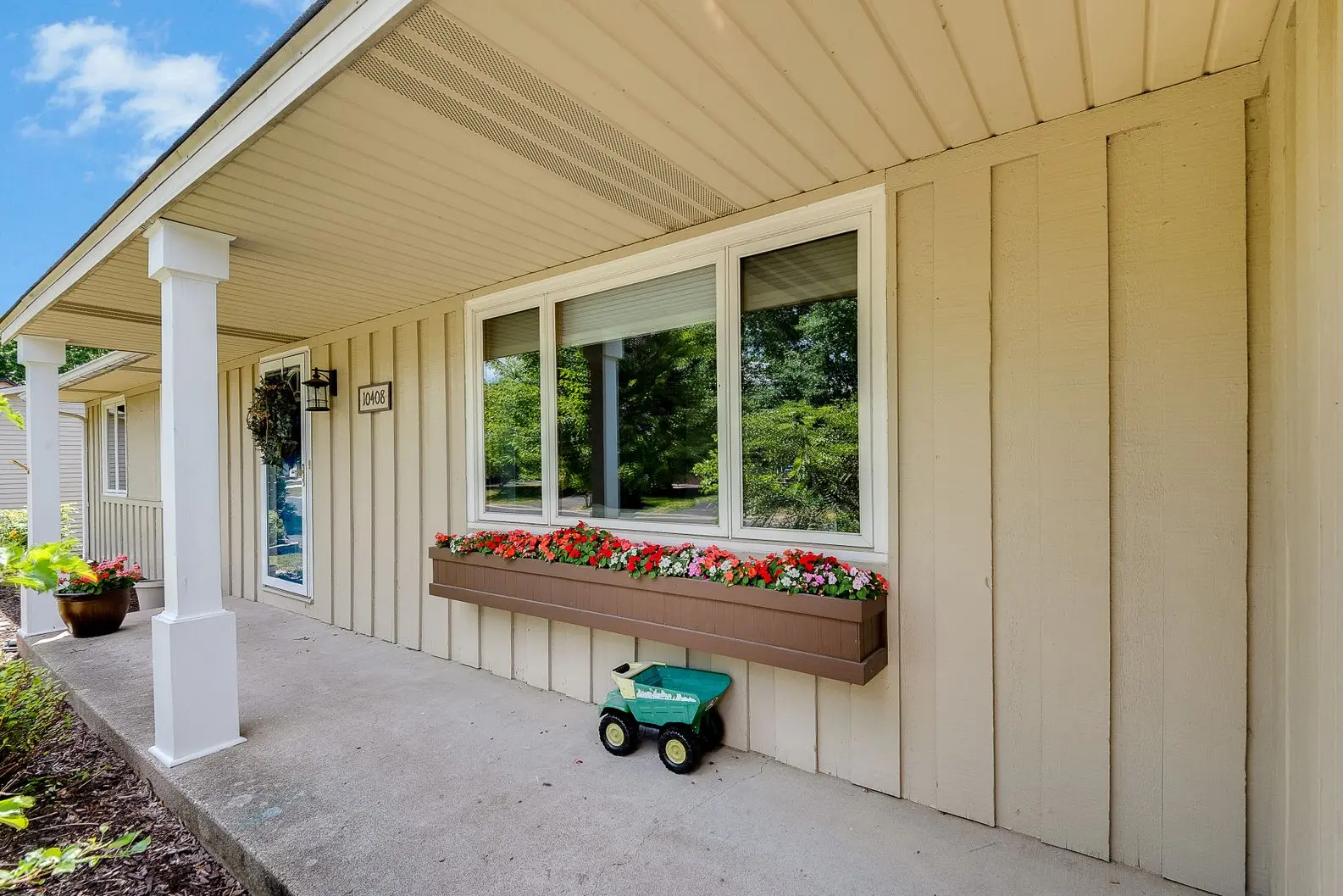 Front porch featuring tan board and batten siding, white window frames, and a brown flower box