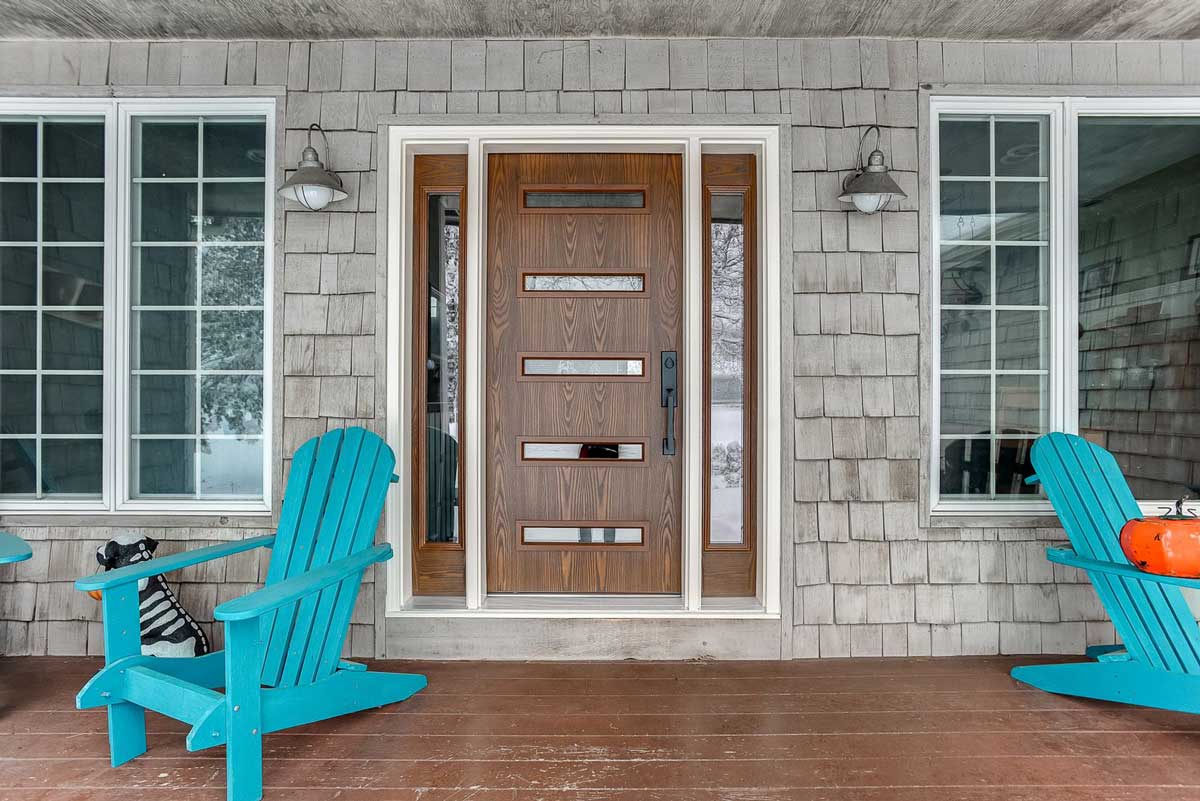 Modern wood front door with horizontal glass windows and sidelights on a cedar shingle house.