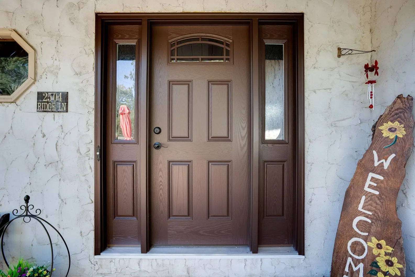 Dark brown front entry door with side windows and a small arched window inset at the top.