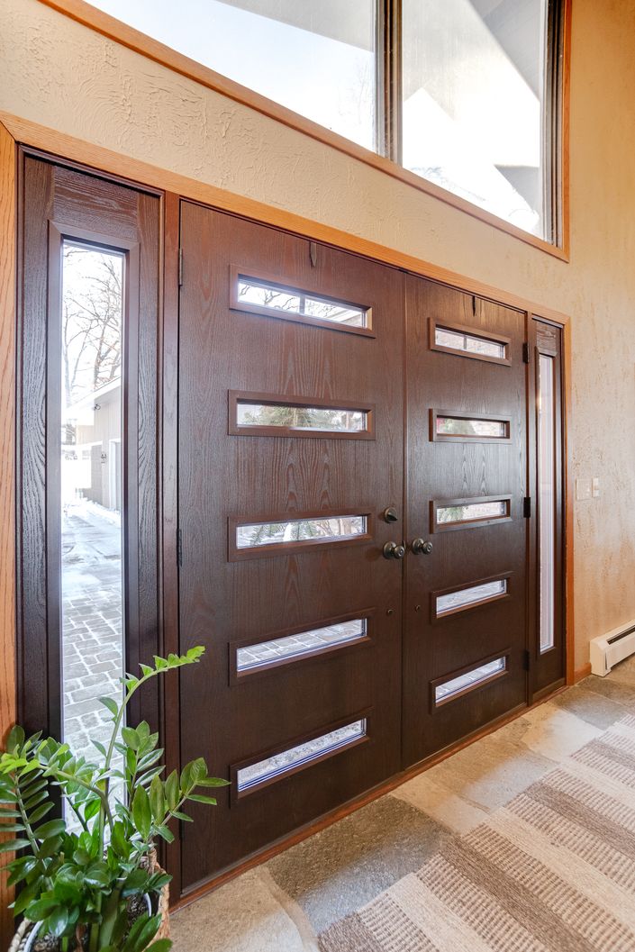 Modern dark wood double entry doors with five horizontal glass lites and vertical sidelights.
